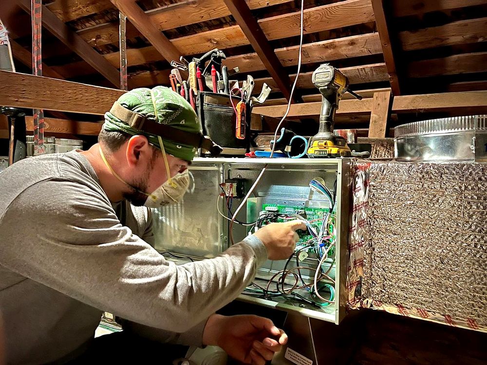 A Pon Air technician working on a furnace control board in a Fontana attic.